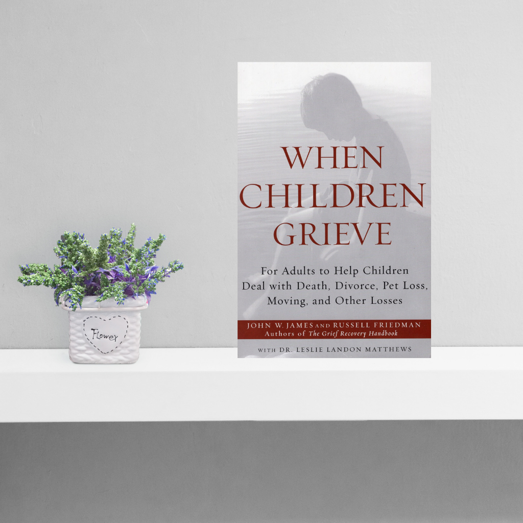 Bogforside med titlen "When children grieve" på hylde ved siden af plante.