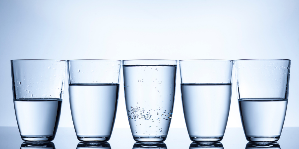 Helt fyldt glas vand i midten ved side af halvt fyldte glas.